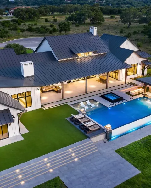 Aerial view of a white farmhouse estate with a glowing pool at dusk