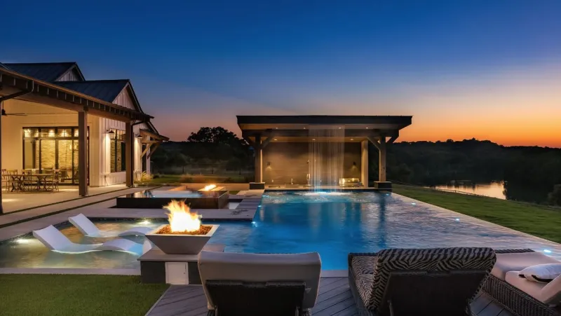 Twilight pool with fire bowls and a waterfall pavilion over a river view