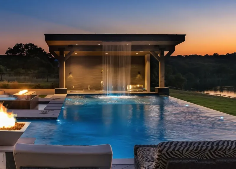 Wide twilight view of a waterfall pavilion and fire features